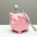 Pink piggy bank and dental tools on gray background. The concept of how to save on dental treatment prodentsearch.com
